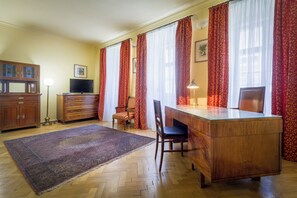 Een kamer met een houten bureau, een televisie, een stoel en een groot raam met rode gordijnen.