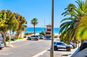 Zona d'aparcament amb cotxes, un edifici amb un rètol i vista a l'oceà.