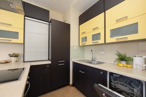 A compact kitchen with black cabinets, a built-in dishwasher, and a window with blinds. - Warsaw | Biały Kamień 2 | Bright apartment | Free Parking (Warszawa)