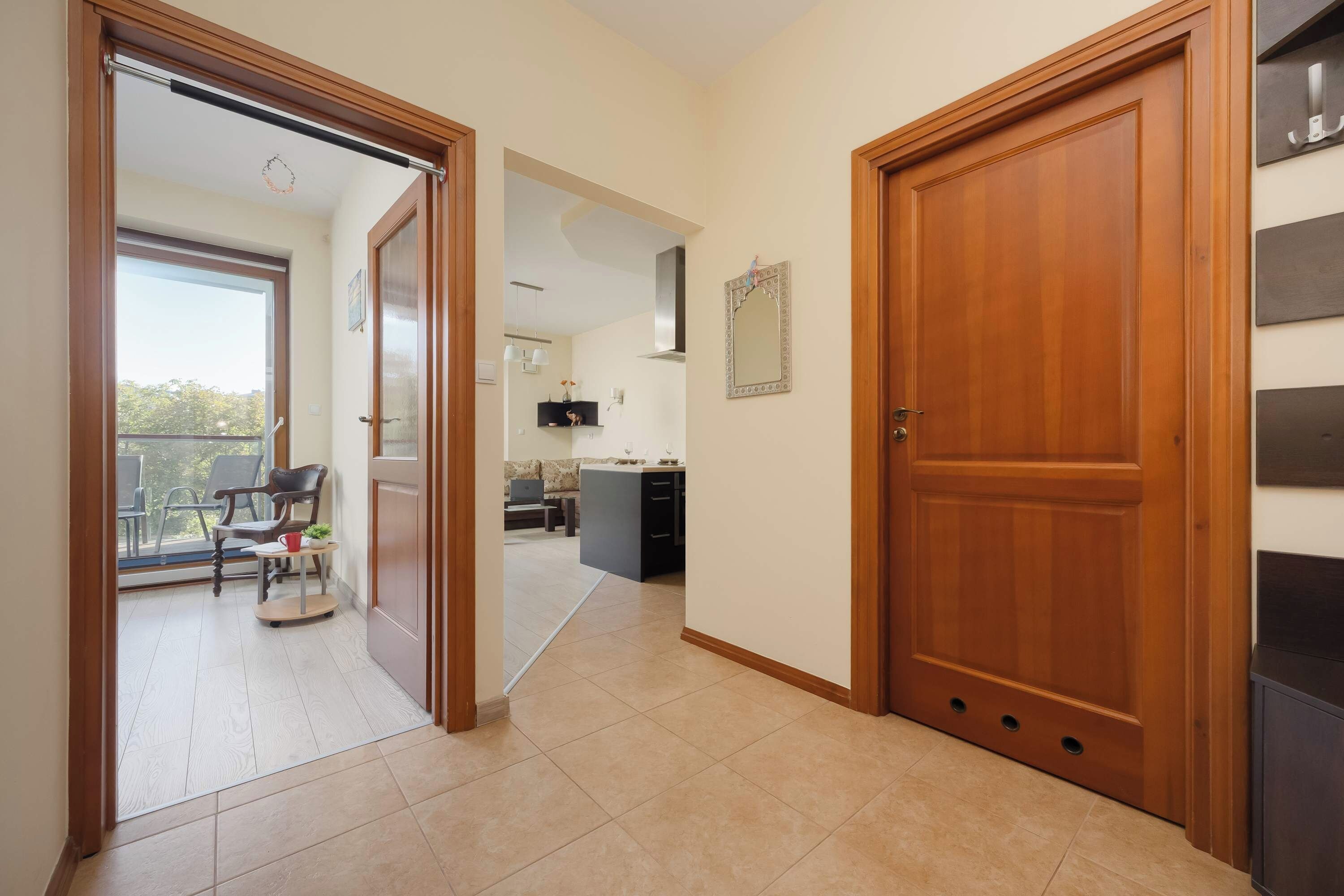 A hallway with a wooden door, a glass door leading to a balcony, and a kitchen area with a dining table and chairs.