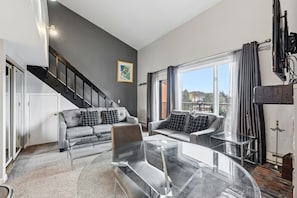 A modern living room with a staircase, grey sofas, and a glass coffee table. - Breckenridge Studio Retreat | Great Location (Breckenridge)
