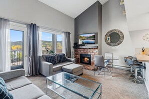 En moderne stue med pejs, en sofa, et glasbord og et spiseområde med barstole.