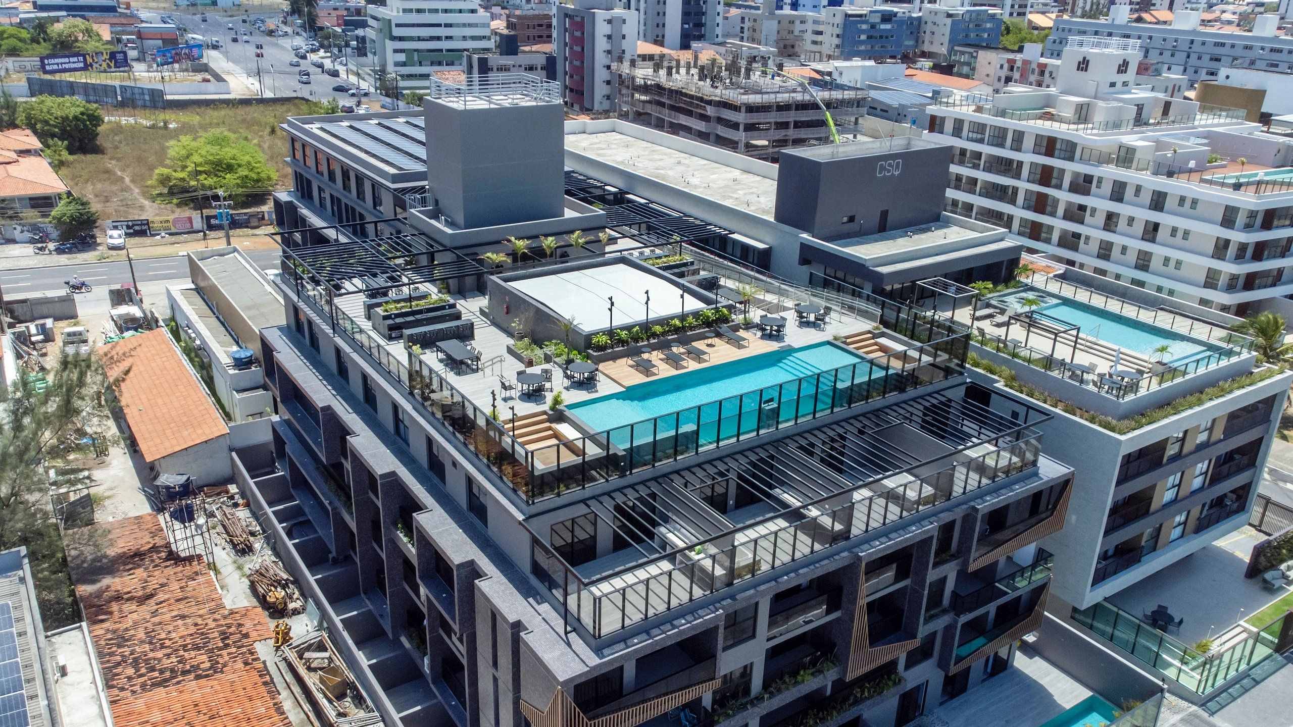 Un edificio moderno con piscina en la azotea, varios balcones y una combinación de espacios comerciales y residenciales.