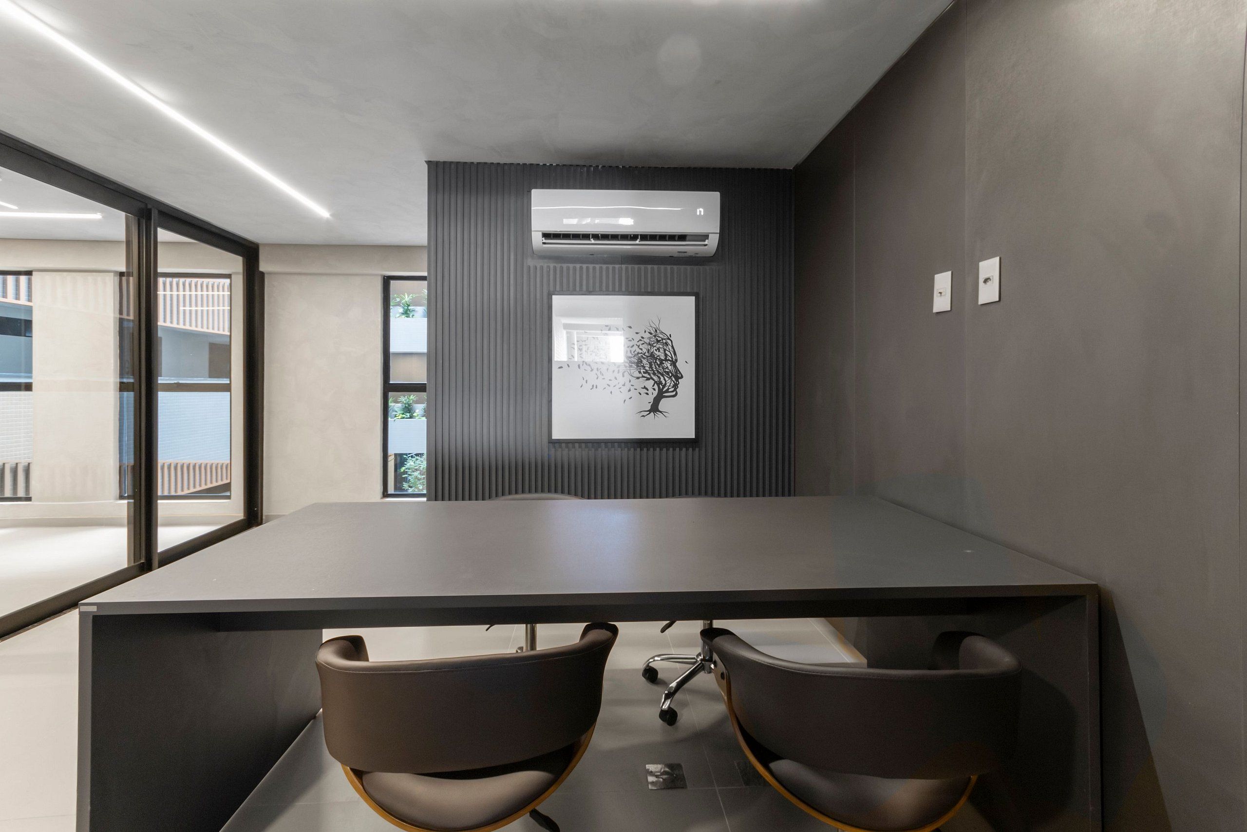 Un salón de conferencias con una larga mesa, dos sillas, un equipo de aire acondicionado y una obra de arte enmarcada en la pared.
