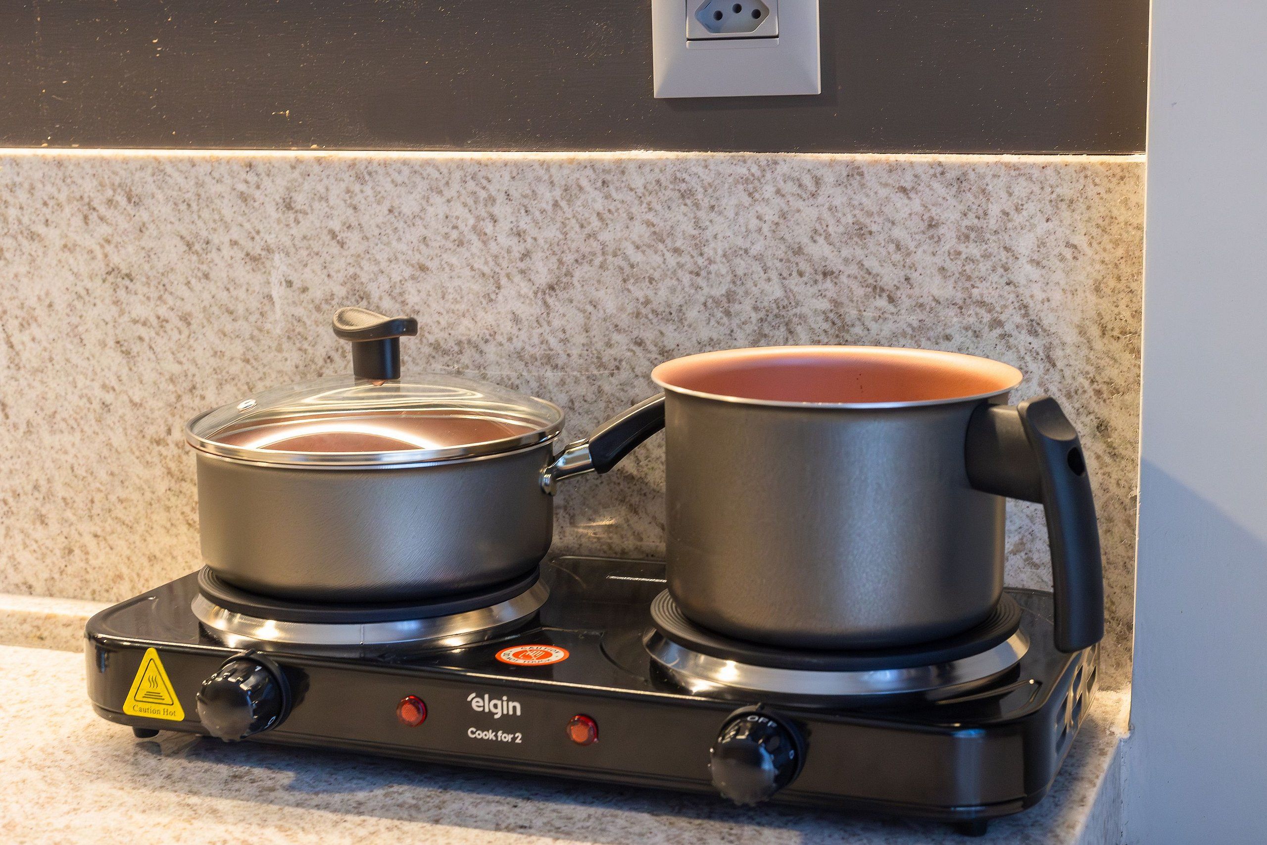 Estufa eléctrica portátil con dos ollas sobre una encimera de cocina.