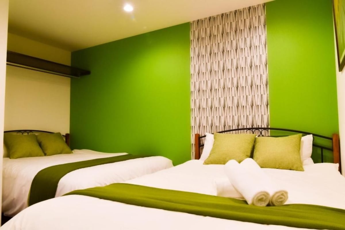 A hotel room with two beds, green walls, and a curtain.