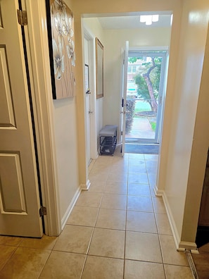 Un couloir avec une porte sur la gauche, un petit banc et une vue sur l’extérieur grâce à une porte vitrée.