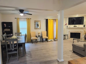A living room with a fireplace, a television mounted above it, and a dining area with a table and chairs. - Virginia Beach Townhome near town center, Mount Trashmore Park and Pembroke Mall (Virginia Beach)