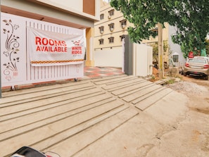 Entrada de hotel com um anúncio de quartos disponíveis, um caminho pavimentado que leva à entrada e um carro estacionado.