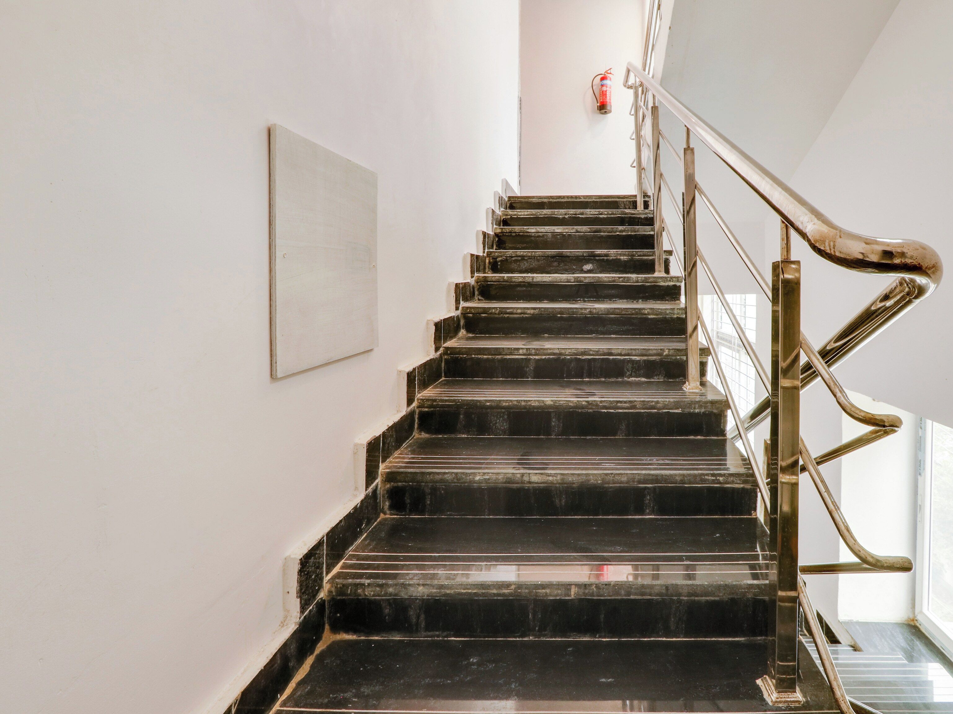 A staircase with black steps and a metal handrail, leading to a landing with a fire extinguisher mounted on the wall.