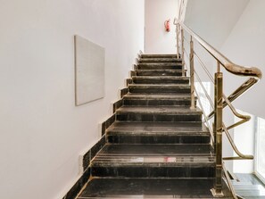 A staircase with black steps and a metal handrail, leading to a landing with a fire extinguisher mounted on the wall. - Collection O White Ridge Kamineni (Hyderabad)