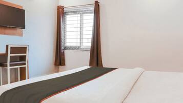 Quarto de hotel com cama, cadeira, janela com cortinas e televisão na parede.