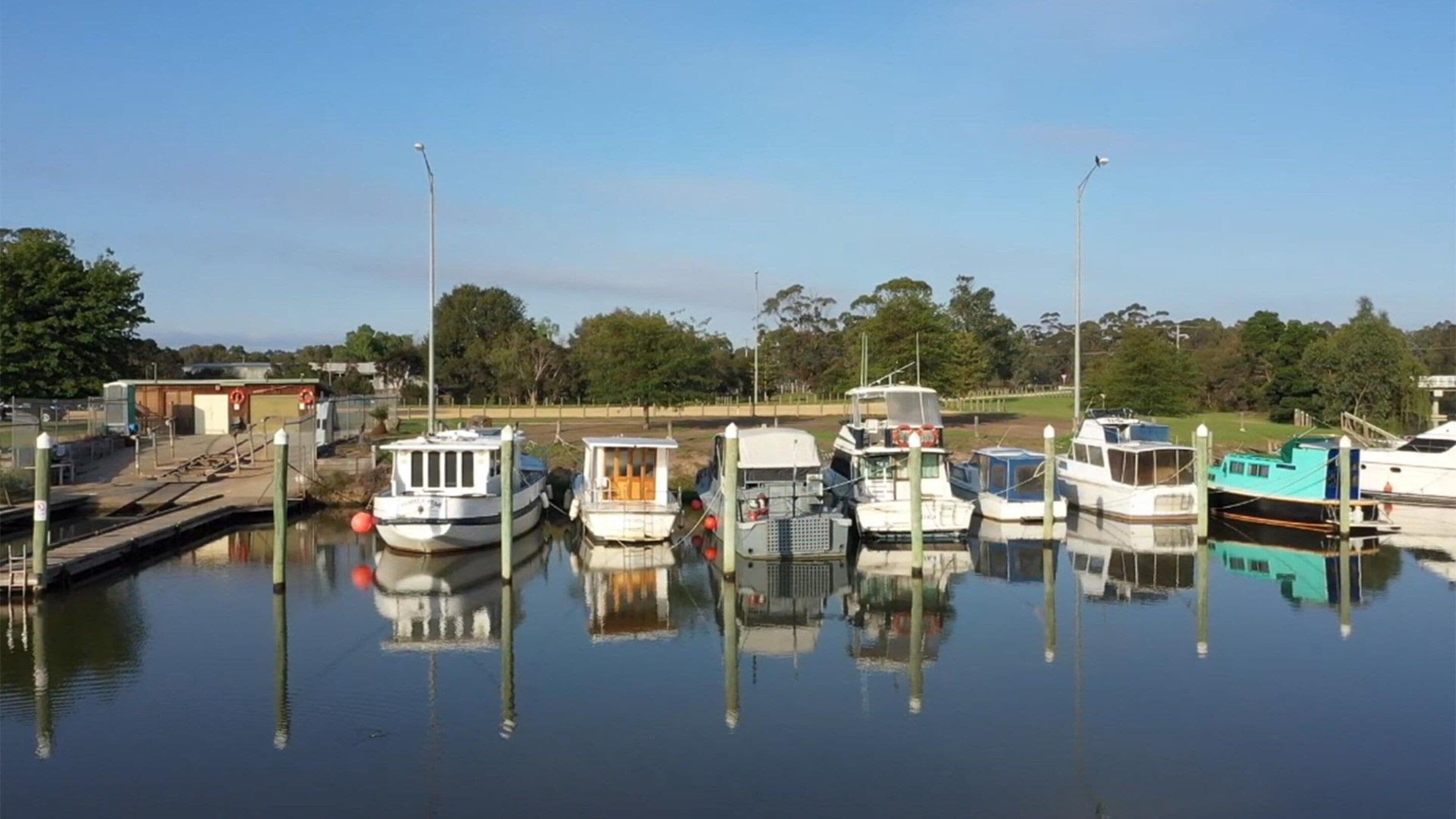 A marina with several boats docked, calm water, and a clear sky.