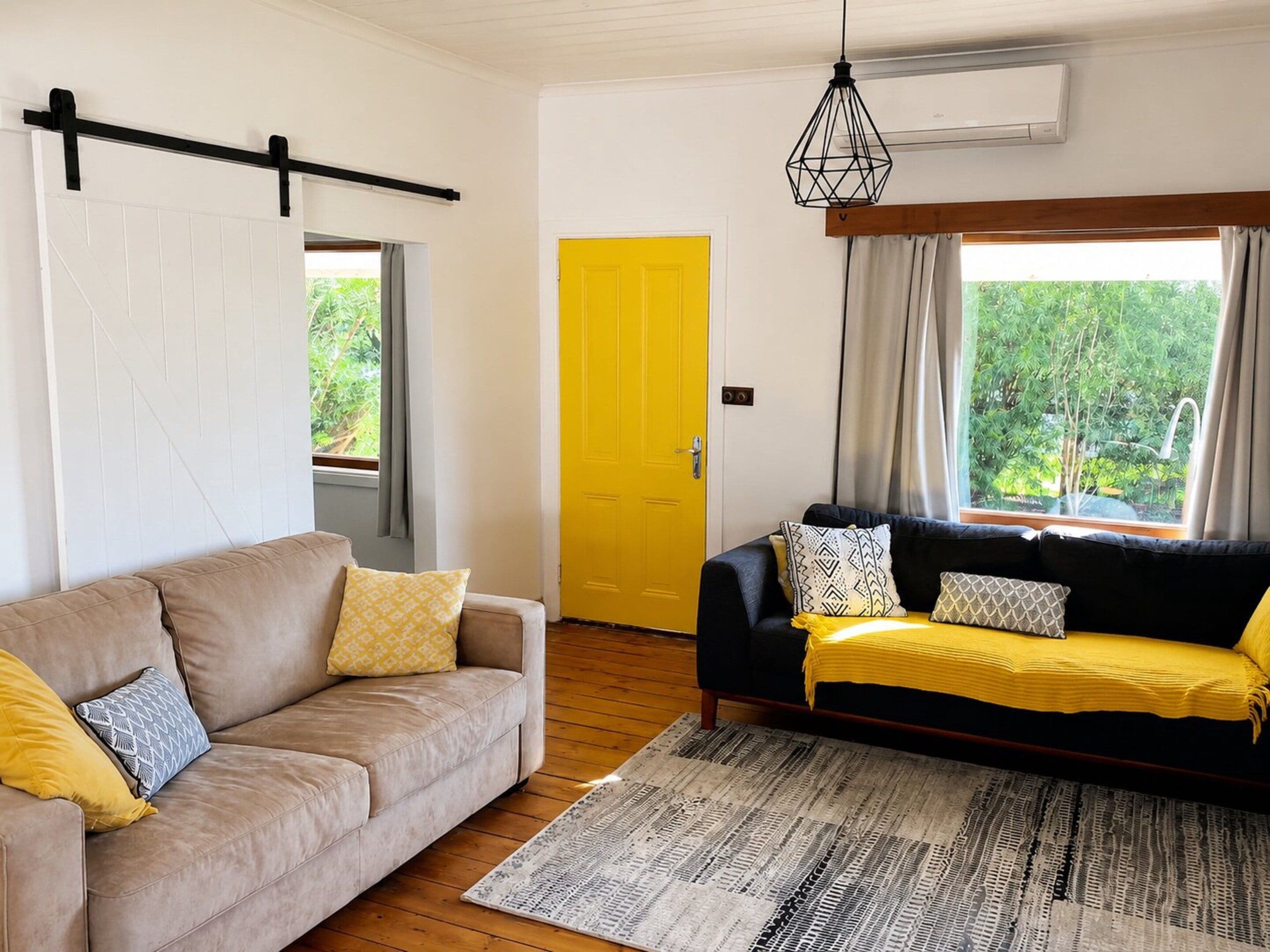 A living room with two sofas, a patterned rug, a yellow door, and a window with curtains.