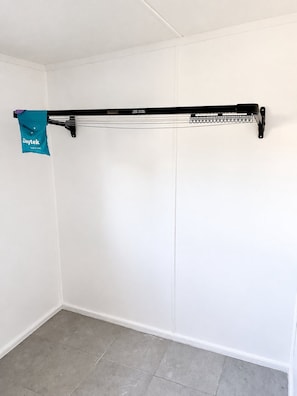 Ein weißer Kleiderschrank mit einer schwarzen Kleiderstange und einer blauen Tasche daran.