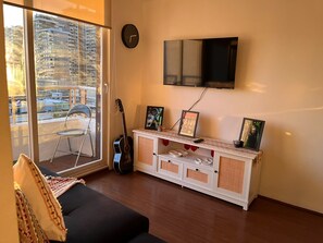 A living room with a sofa, a TV mounted on the wall, a guitar, and a cabinet with decorative items. - 2-bedroom/2-bathroom apartment near Movistar/Metro + Pool (Santiago)