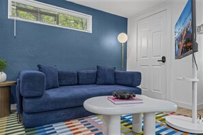 A room with a blue sofa, a white table with a bowl, a potted plant, a white door, and a painting on the wall. - Tarrytown Loft | Private Patio + Workspace (Austin)