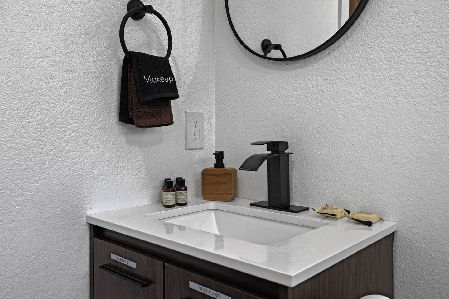 A bathroom with a white sink, a black faucet, a towel ring with a brown towel, and a mirror.