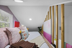 A bedroom with a sloped ceiling, a bed with multiple pillows, a bedside table, and a wall with vertical wooden panels. - Tarrytown Loft | Private Patio + Workspace (Austin)