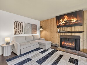 A living room with a fireplace, a sofa, a rug, and wall art. - Summit Nook | 2 bdrm Brian Head Condo (Brian Head)