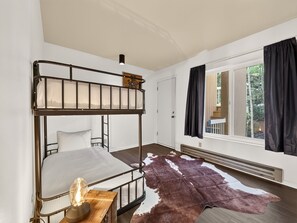 A bunk bed room with a cowhide rug, a heater, and a window with curtains. - Summit Nook | 2 bdrm Brian Head Condo (Brian Head)