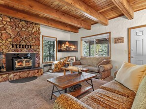 A cozy cabin interior with a stone fireplace, a sofa, a coffee table, and a television mounted on the wall. - Old Tymer Retreat nestled in the mountains (Duck Creek Village)