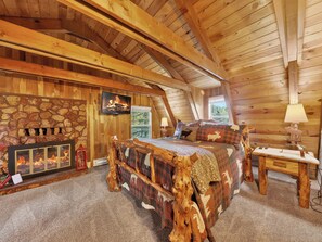 A log cabin bedroom with a stone fireplace, a bed with animal-themed bedding, and a television mounted on the wall. - Old Tymer Retreat nestled in the mountains (Duck Creek Village)