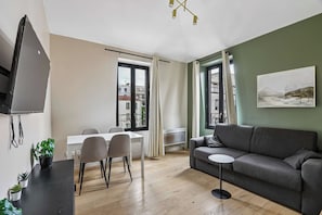 Una sala de estar moderna con un sofá gris, una mesa de comedor con sillas, un televisor montado en la pared y un cuadro en la pared.