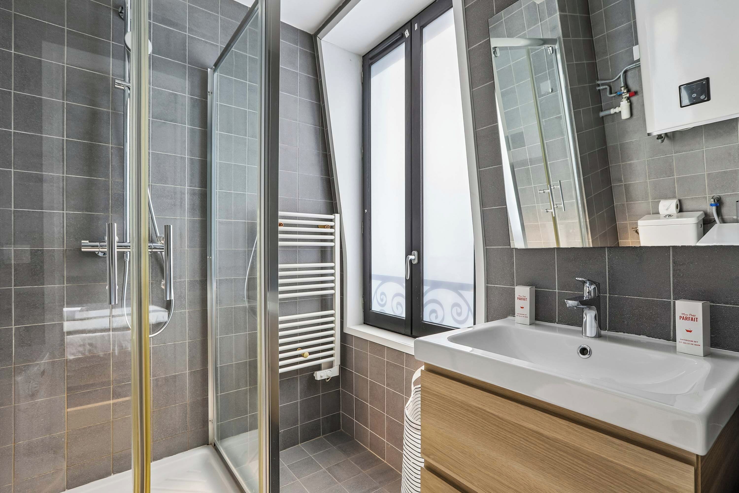 A modern bathroom with a glass shower enclosure, a large mirror, and a white sink with a wooden vanity.
