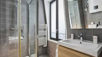 A modern bathroom with a glass shower enclosure, a large mirror, and a white sink with a wooden vanity.