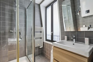 A modern bathroom with a glass shower enclosure, a large mirror, and a white sink with a wooden vanity. - Cozy 1BR Retreat for Couples & Families (Boulogne-Billancourt)