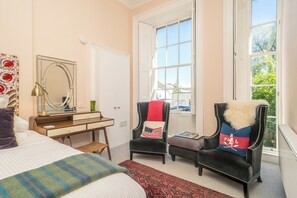 Een slaapkamer met een bed, een bureau, twee stoelen, een raam en een deur.