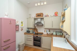 Een kleine keuken met een roze koelkast, een magnetron, een fornuis en een spoelbak.
