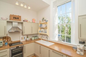 A kitchen with white cabinets, a stainless steel range hood, a double oven, a sink, and a window with a view of trees. - Elegant 3BR Georgian Gem in Central Edinburgh - Pass the Keys (Edinburgh)