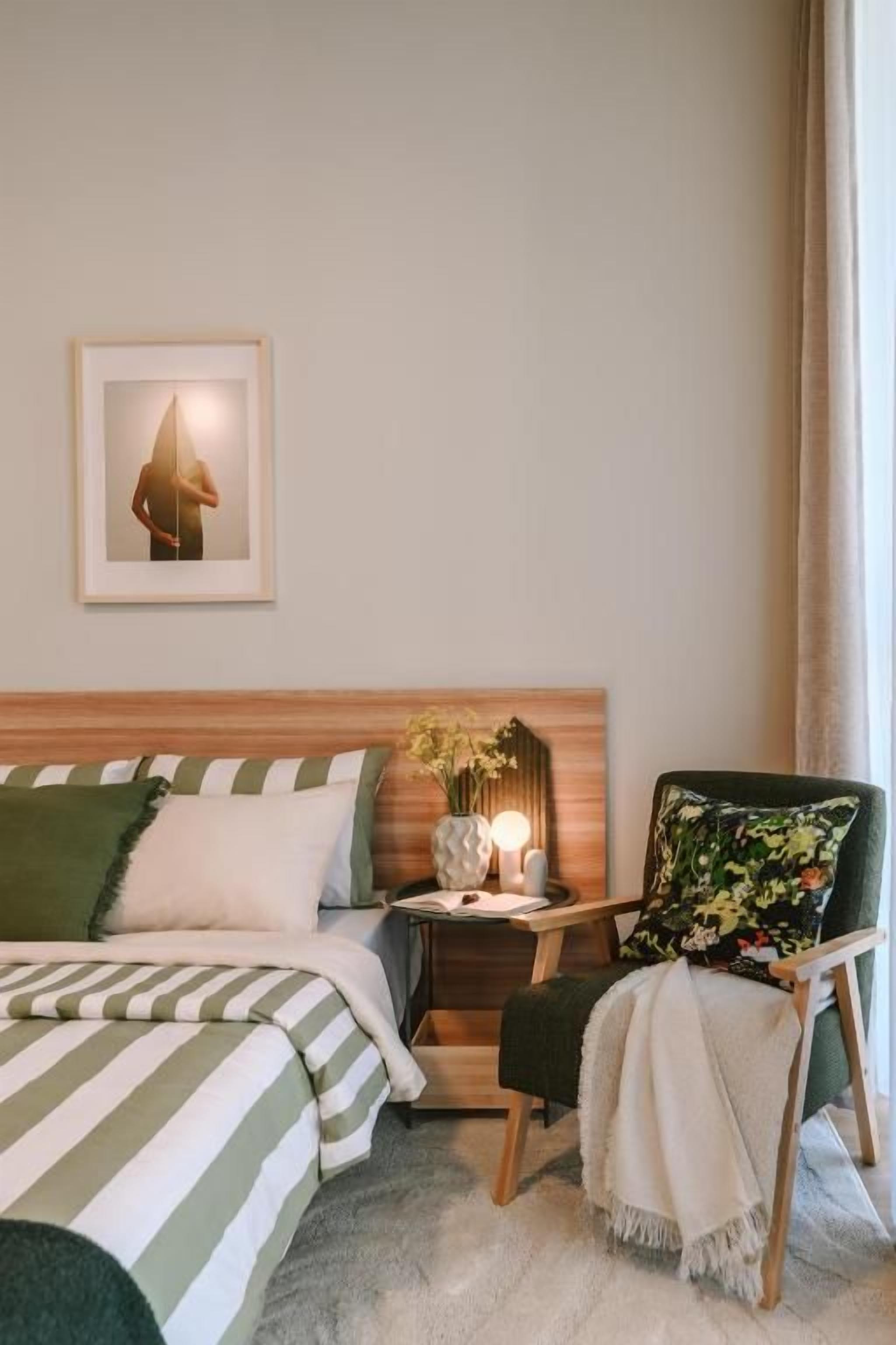 Una camera d'albergo con un letto, una sedia, un comodino e un quadro appeso al muro.