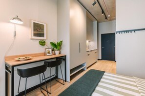 A compact living space with a kitchenette, a bed with striped bedding, a small dining area with a table and chairs, and a potted plant.