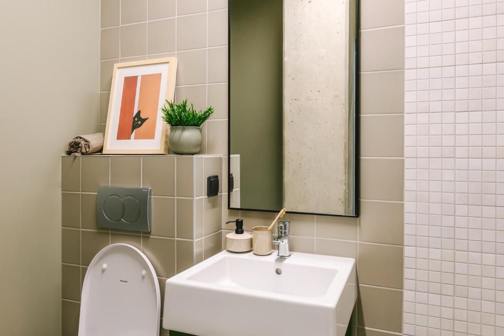 Un baño con lavamanos blanco, inodoro, un cuadro enmarco, una planta pequeña y un espejo.