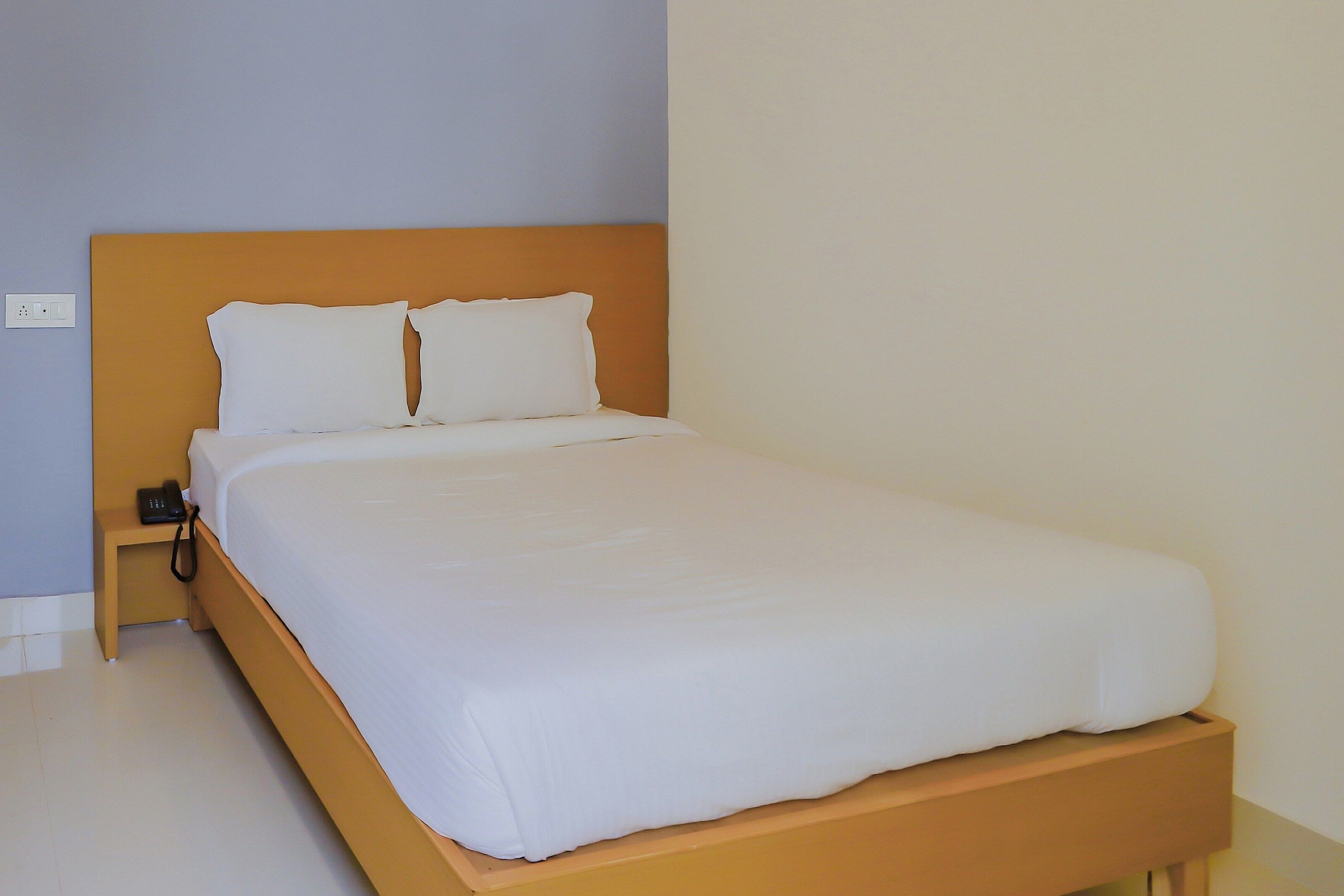 Una cama individual con cabecera de madera y ropa de cama blanca en una habitación con paredes de tonos claros.