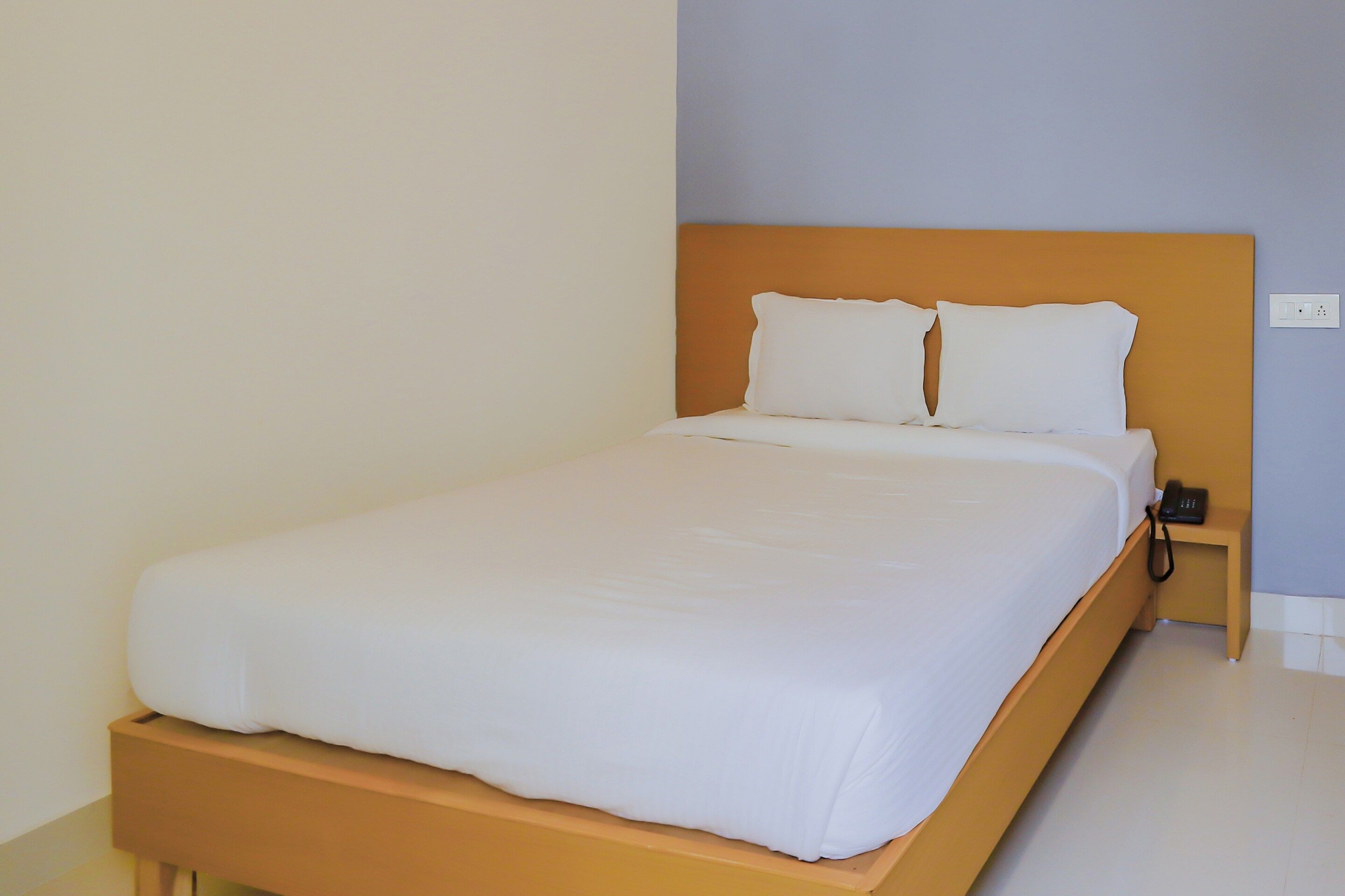 A single bed with a wooden headboard and white bedding in a room with light-colored walls.