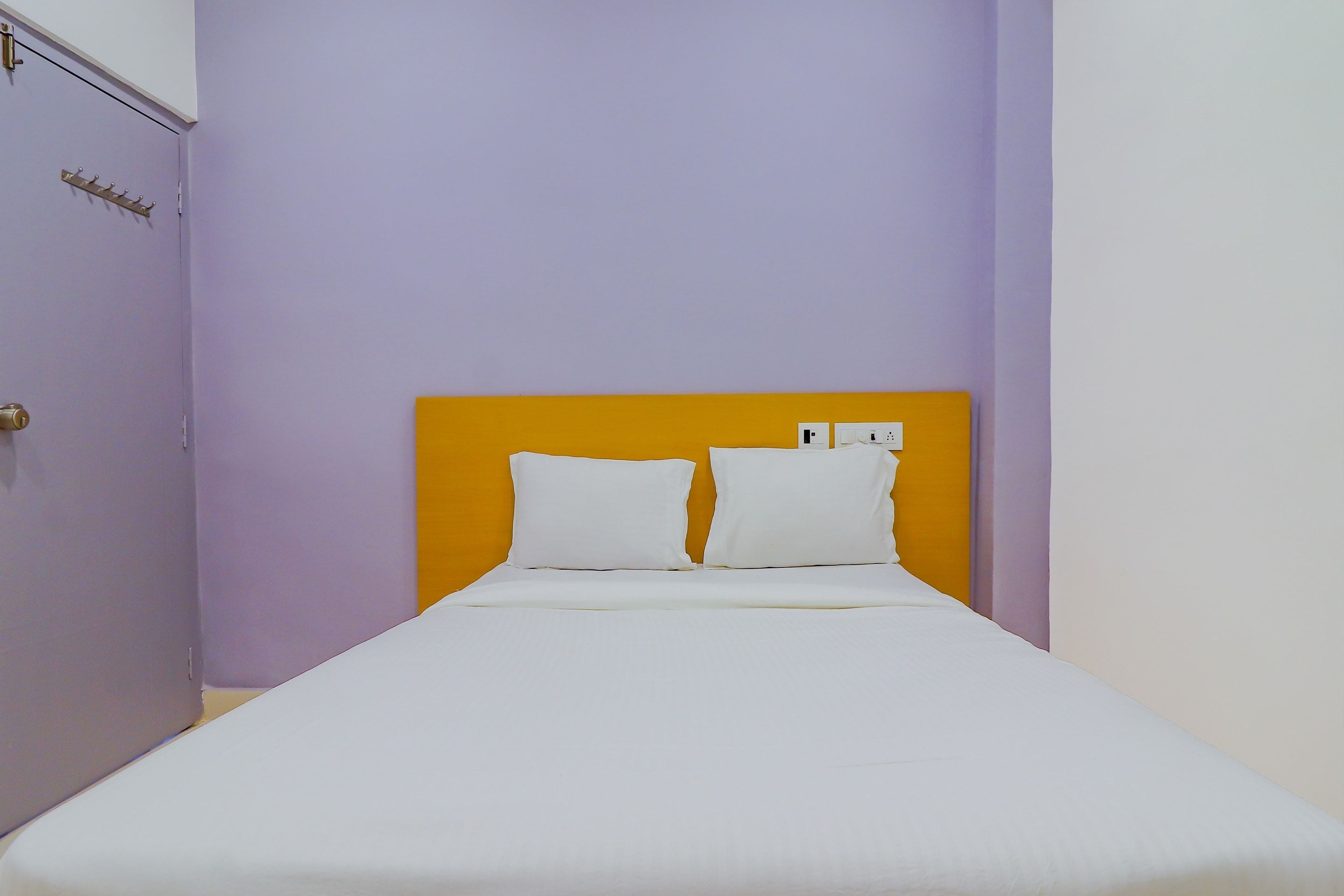 Una cama individual con ropa blanca y un cabecero naranja en una habitación con paredes moradas.