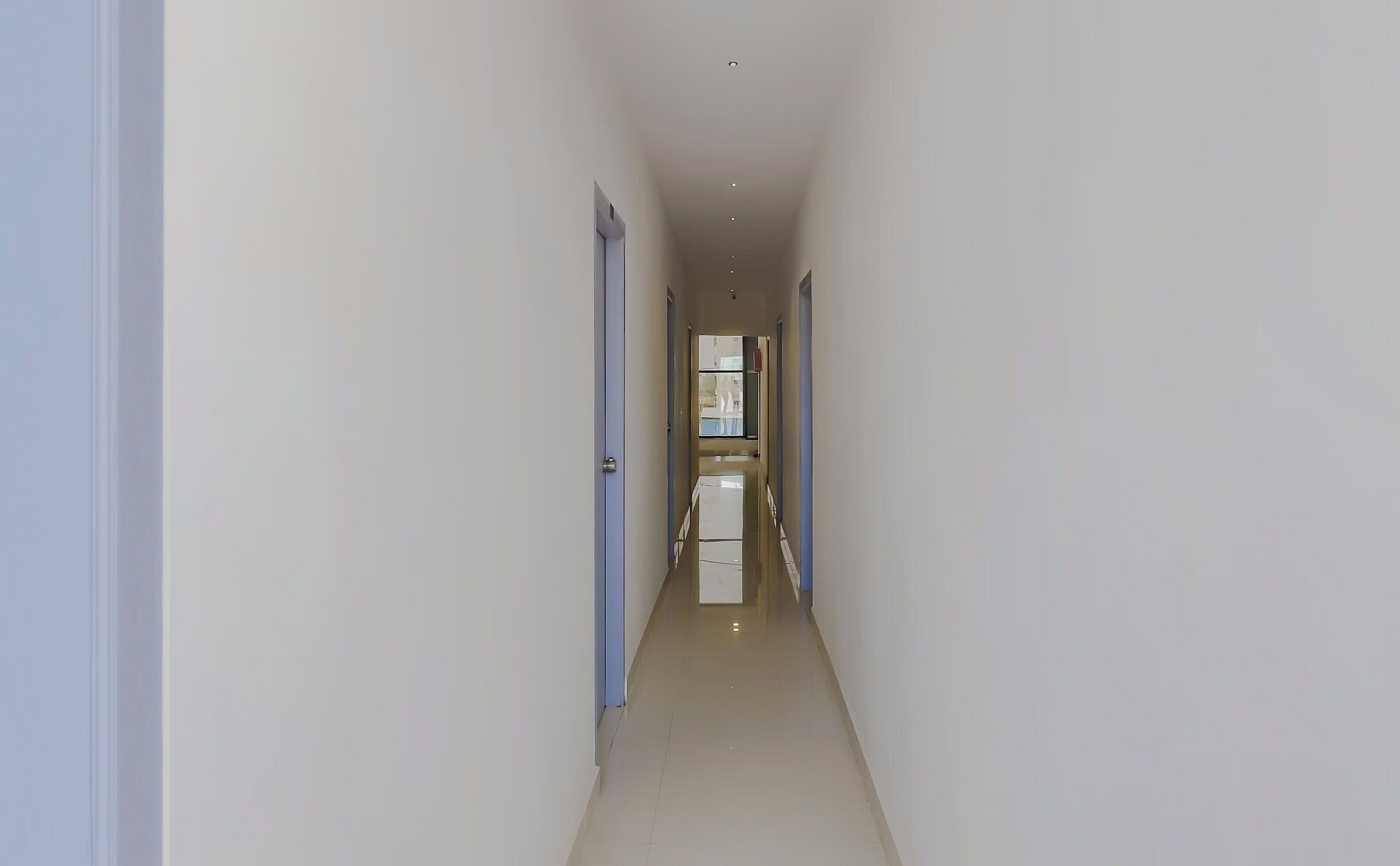 A narrow, well-lit hallway with a door on the left and a window at the end.