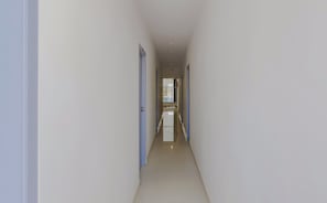 Un pasillo estrecho y bien iluminado, con una puerta a la izquierda y un ventanal al final.