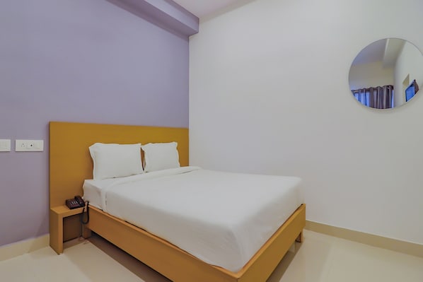 Una cama individual con estructura de madera y ropa de cama blanca en una habitación con paredes moradas claras y suelo blanco.