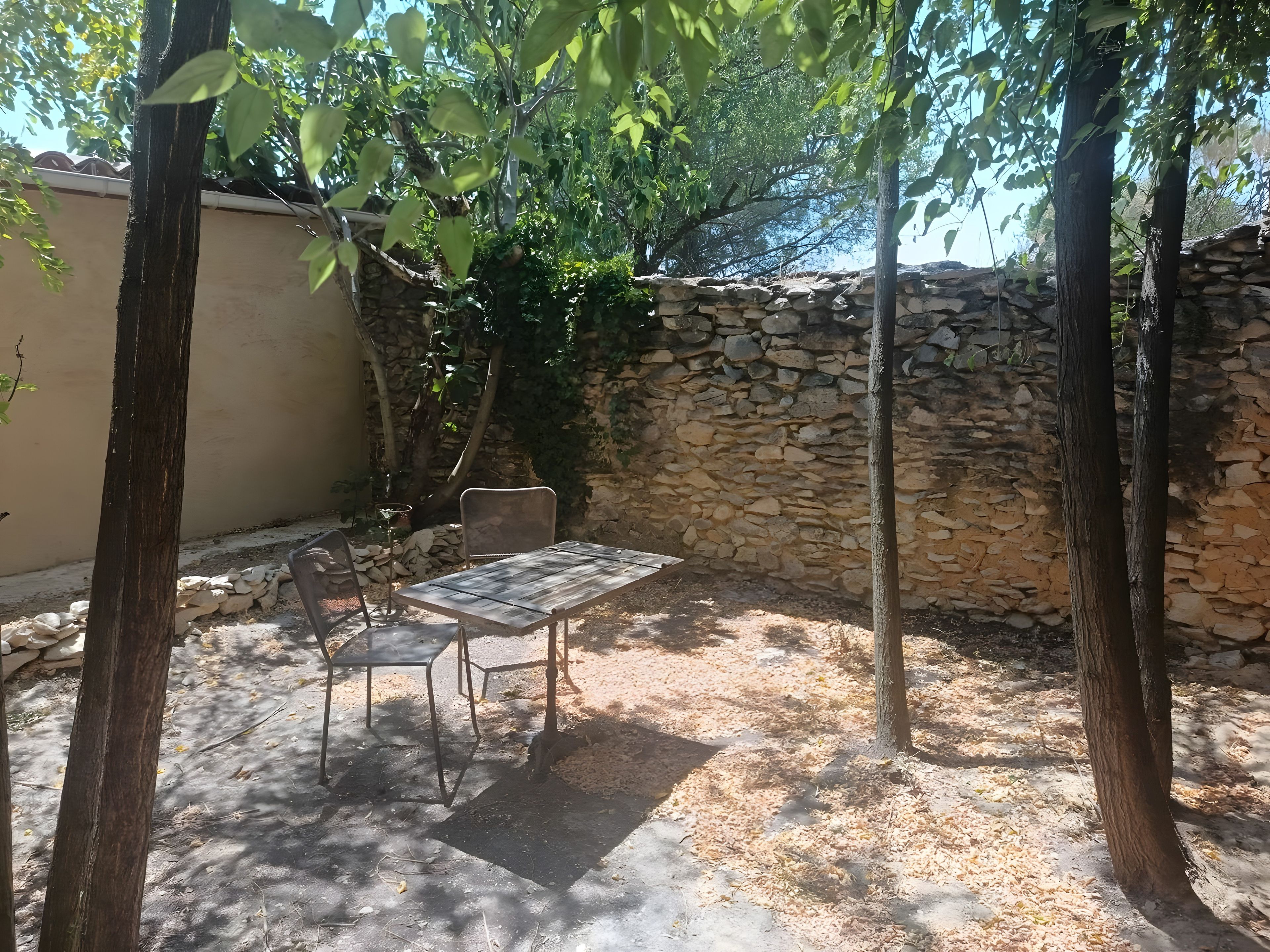 An outdoor patio with a table and chairs, surrounded by trees and a stone wall.