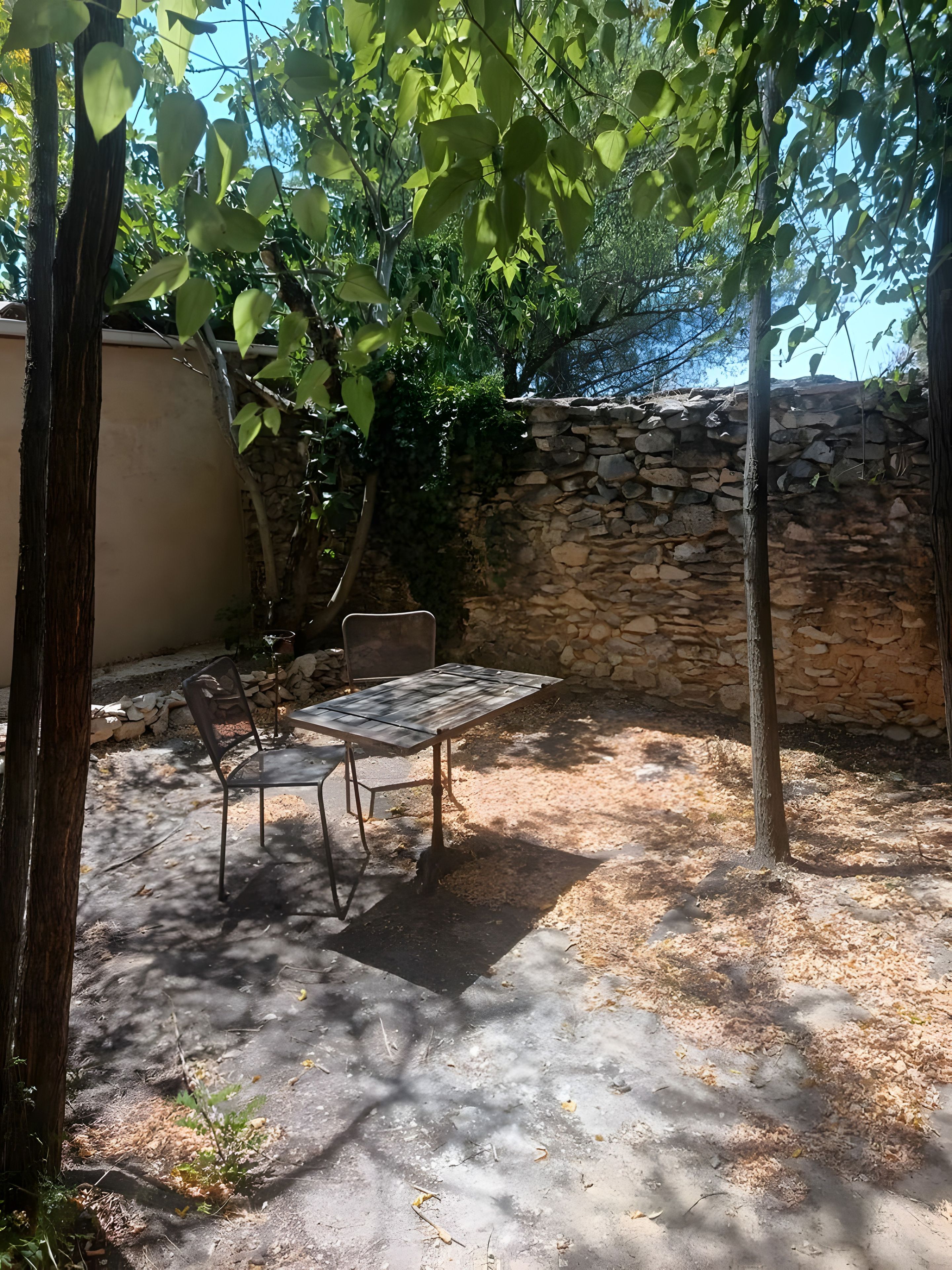 An outdoor patio with a table and chairs, surrounded by trees and a stone wall.