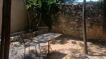 An outdoor patio with a table and chairs, surrounded by trees and a stone wall.