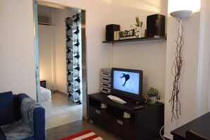A living room with a television, a sofa, a coffee table, and a decorative plant. - Clio's Beach House - Deluxe Beach front property (Ormos Korthiou)