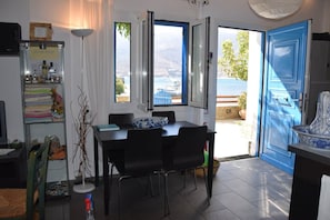 A dining area with a table and chairs, a view of the sea through open doors, and a blue door. - Clio's Beach House - Deluxe Beach front property (Ormos Korthiou)