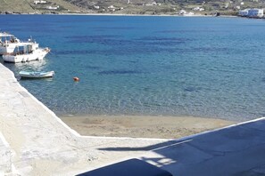 A coastal scene with boats docked near a sandy beach, clear water, and a hilly landscape in the background. - Clio's Beach House - Deluxe Beach front property (Ormos Korthiou)