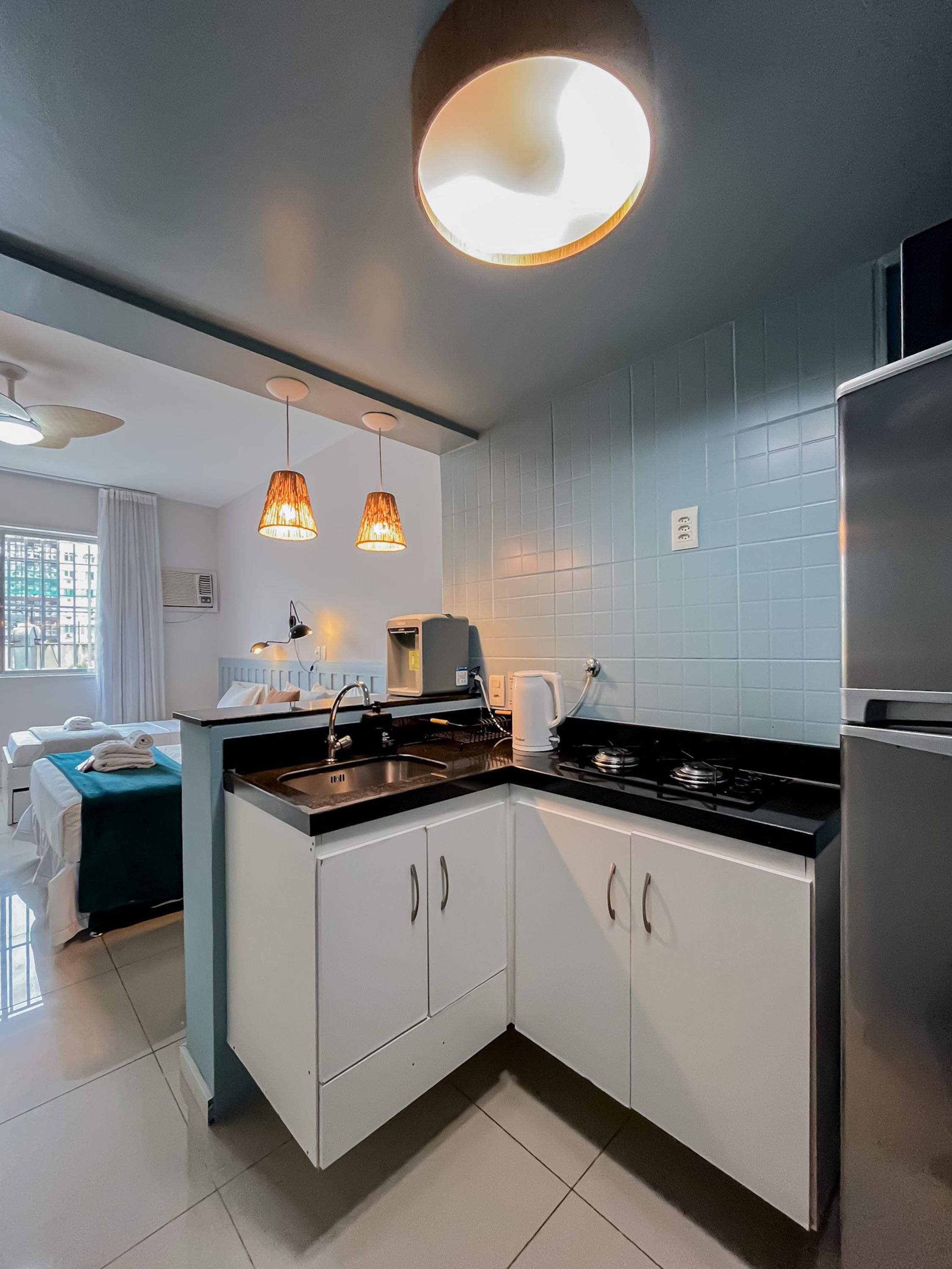 Una cocina moderna con armarios blancos, un refrigerador de acero inoxidable y una estufa a gas. Hay dos lámparas colgantes con una luz cálida.